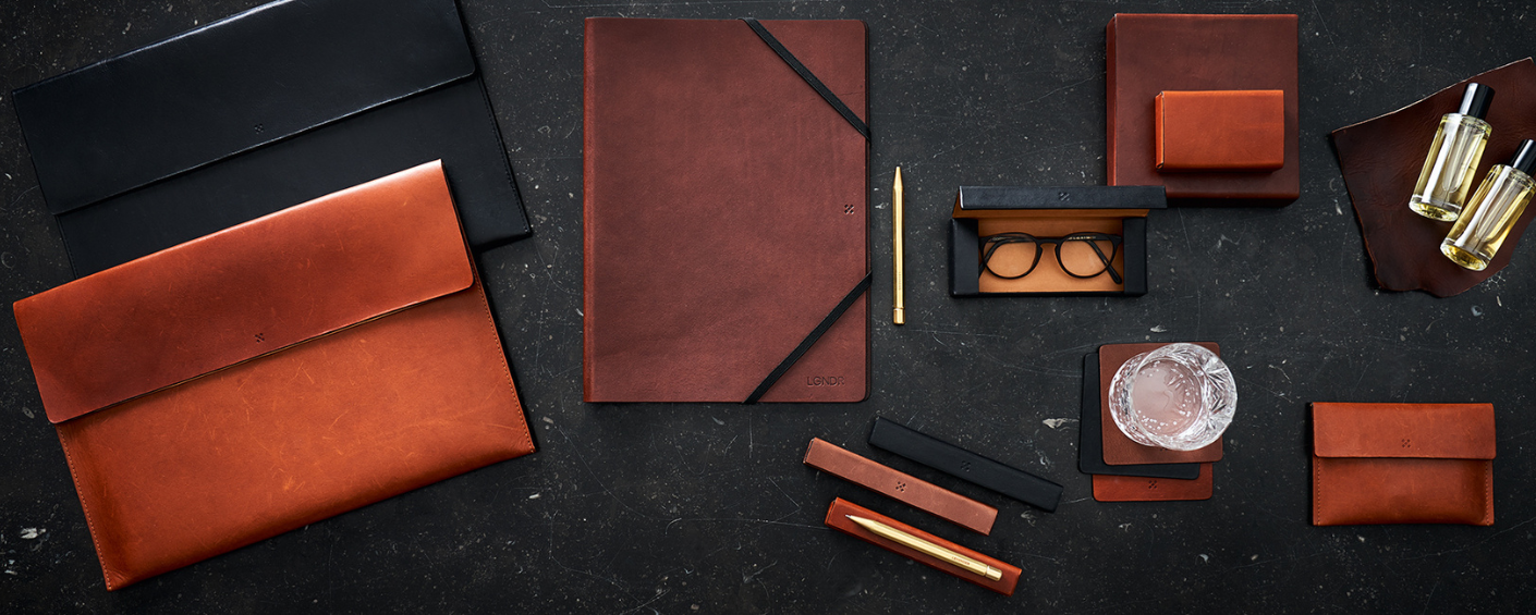 Legendär Accessoires – Lederprodukte & Parfums im Flatlay auf dunklem Untergrund Lederaccessoires und Parfums von Legendär – Briefmappen, Notizbuchhüllen, Etuis und Flakons auf dunklem Hintergrund im Flatlay-Stil